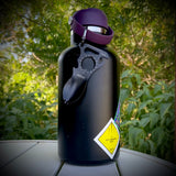 A tactical spork hangs from a big black metal water bottle with purple lid.  Assorted stickers adorn the bottle.